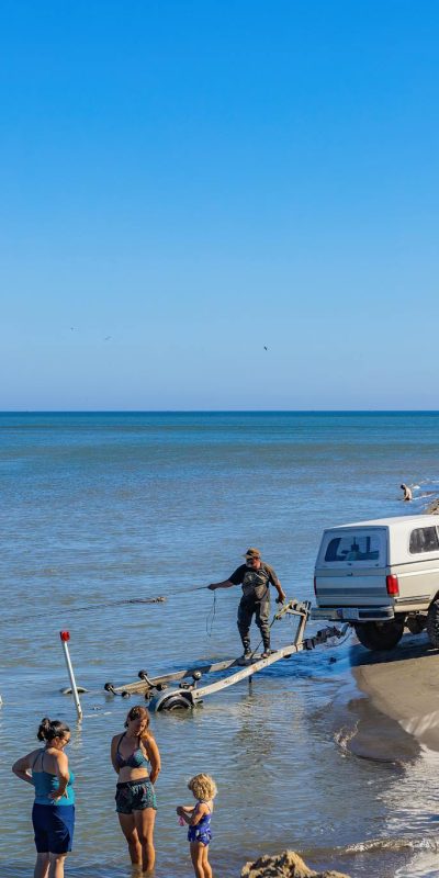 A Person Standing on Trailer Pulling a Boat on Body of Water